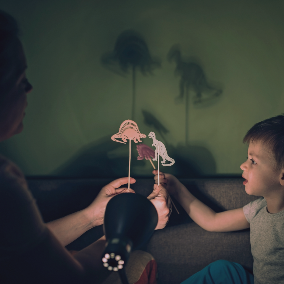 Adult and child moving dinosaur outlines on a stick in front of a projection unit