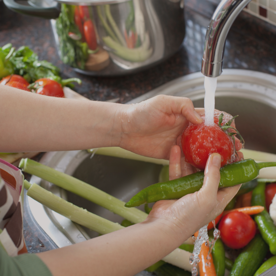 Hands washing a tomato under a faucet of running water.