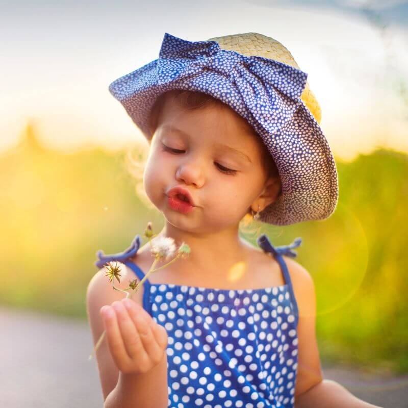 Little girl blowing at a flower